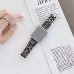 Ceramics replacement strap for Apple Watch, featuring a rhombic grid pattern, placed on a magazine with a hand visible.