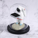 Decorative watch display stand featuring a small astronaut holding a black platform under a glass dome.